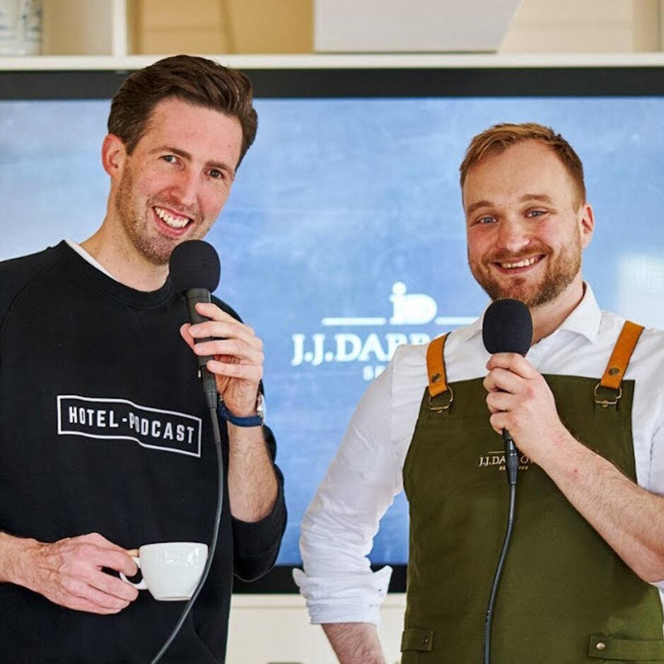 Podcast hosts discussing hospitality trends in the stylish J.J. DARBOV hotel setting with microphones and coffee cups.