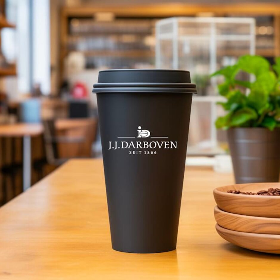 Reusable coffee cup on a café table, featuring the J.J. Darboven logo, with coffee beans in wooden bowls nearby.
