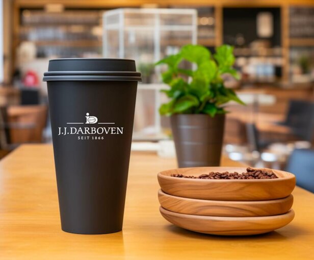 Tasse à café réutilisable sur une table de café, portant le logo de J.J. Darboven, avec des grains de café dans des bols en bois à proximité.