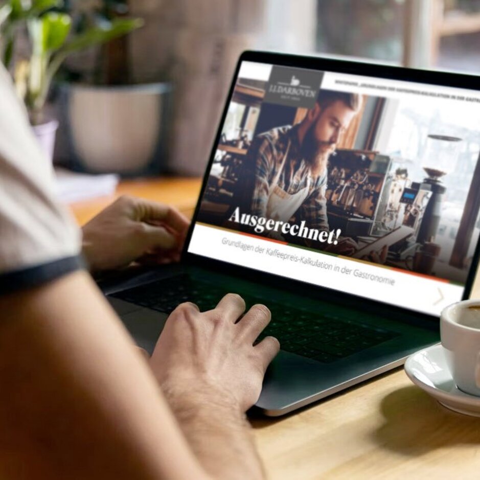 Person, die in einem hellen, einladenden Café mit einem Laptop und einer Kaffeetasse auf dem Tisch die Kaffeepreise berechnet.