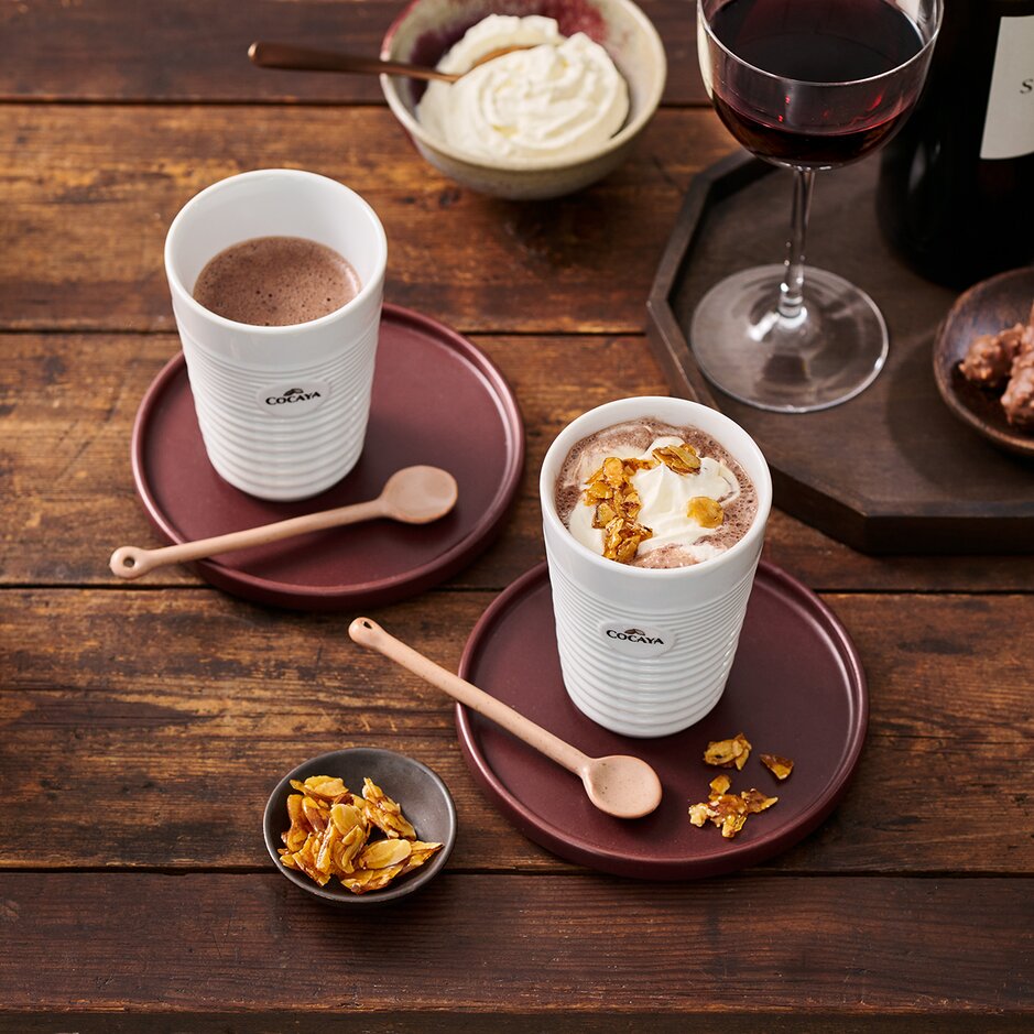 Köstliche Cocaya-Schokoladengetränke mit Toppings, gepaart mit dunklem Rotwein und süßen Leckereien auf einem rustikalen Holztisch.
