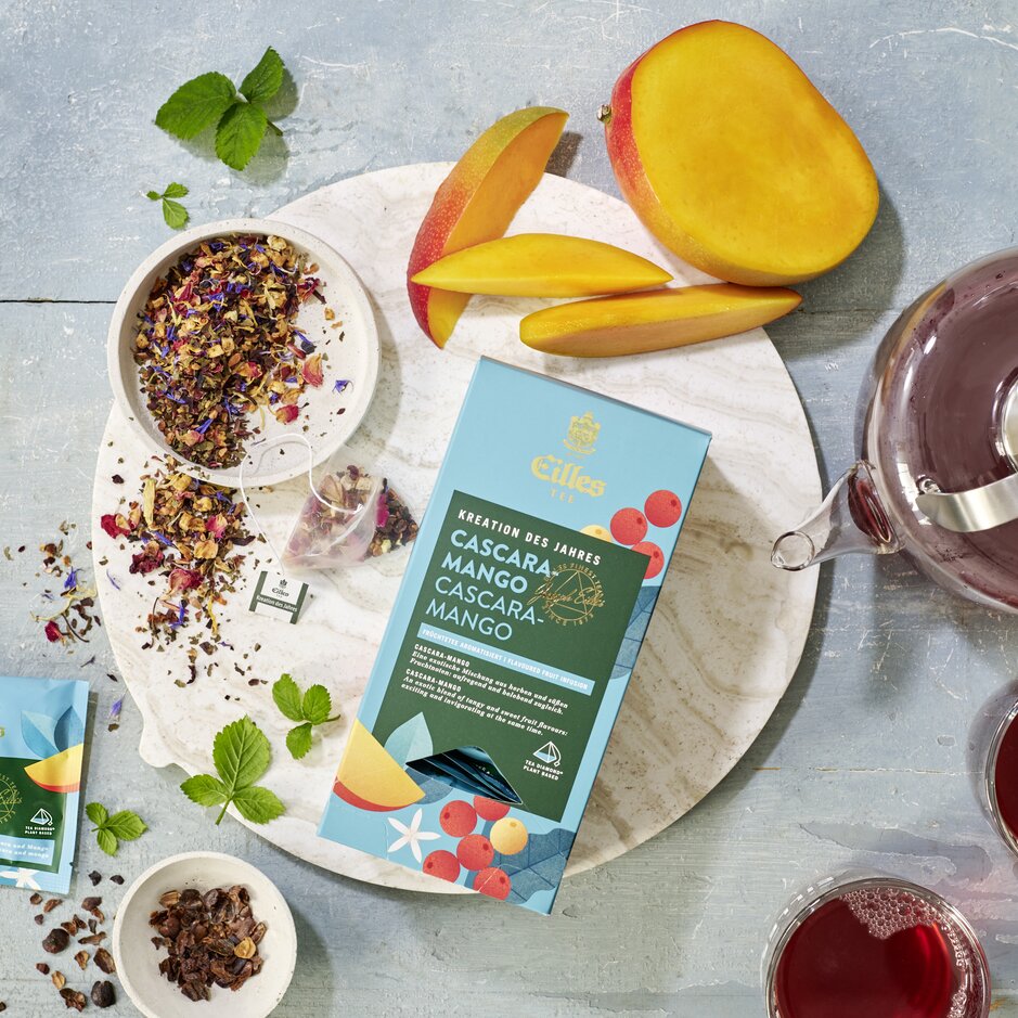 Cascara Mango-Tee mit getrockneten Früchten, frischen Mangoscheiben und aufgebrühtem Tee in einer lebendigen, einladenden Umgebung.