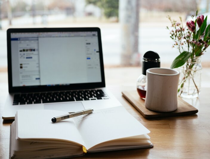 Gezellige werkplek met een laptop, notitieblok, pen, koffiemok en bloemen, perfect voor productiviteit en creativiteit.
