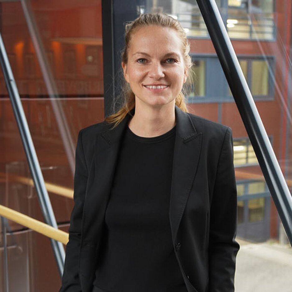 Professional woman in a black blazer stands confidently in a modern office, highlighting the intersection of sustainability and digitalisation.