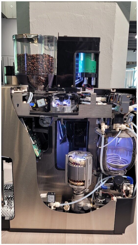 Schnittansicht einer Kaffeemaschine, die die internen Komponenten wie Motor, Wassersystem und Bohnenbehälter zeigt.