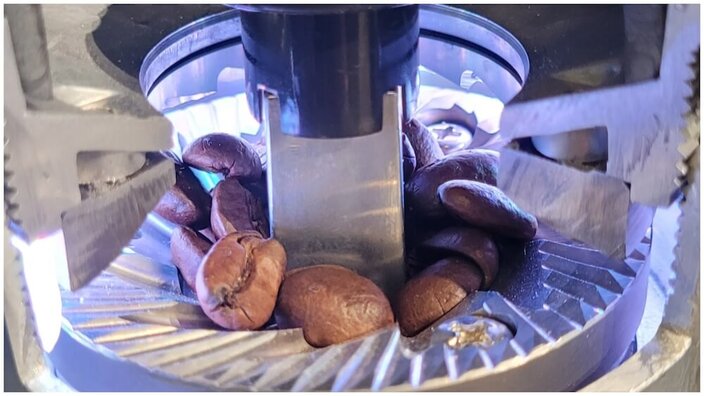 Freshly roasted coffee beans being ground in a coffee grinder, showcasing precision grinding and rich aroma.