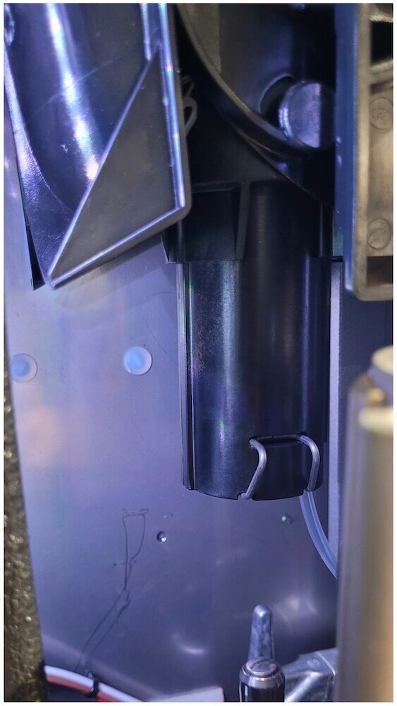 Nahaufnahme der inneren Komponenten eines Geräts, die eine schwarze Röhre, eine Klemme und eine Verdrahtung innerhalb eines Metallgehäuses zeigen.