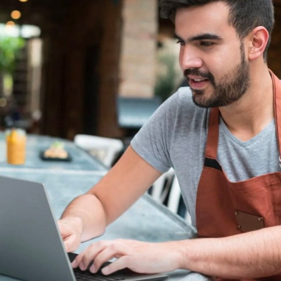 A restaurant staff member uses a laptop in a modern café, embracing digital transformation in the hospitality industry.