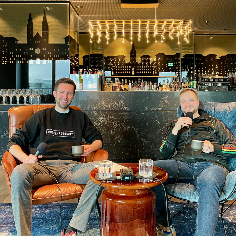 Podcasters enjoying coffee in a stylish hotel bar, with a trendy backdrop and a relaxed atmosphere.