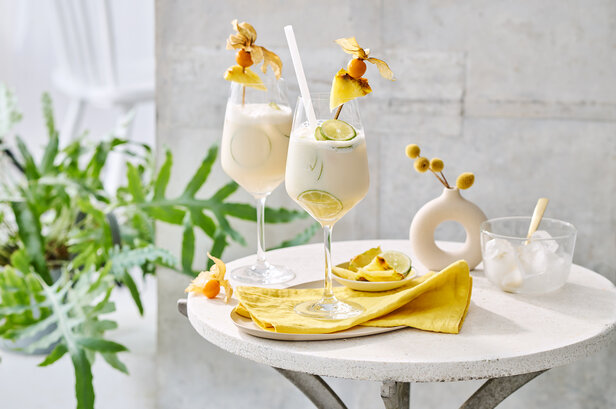 Zwei elegante Pina-Colada-Cocktails, garniert mit Ananas und Limetten, serviert auf einem stilvollen Tisch mit Grünzeug.