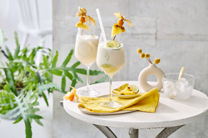 Two elegant pina colada cocktails garnished with pineapple and lime, served on a stylish table with greenery.