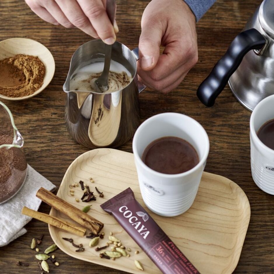 Zubereitung von köstlichen Cocaya-Schokoladengetränken mit frischen Gewürzen und Kakao an einem rustikalen Holztisch. Perfekt für gemütliche Momente.