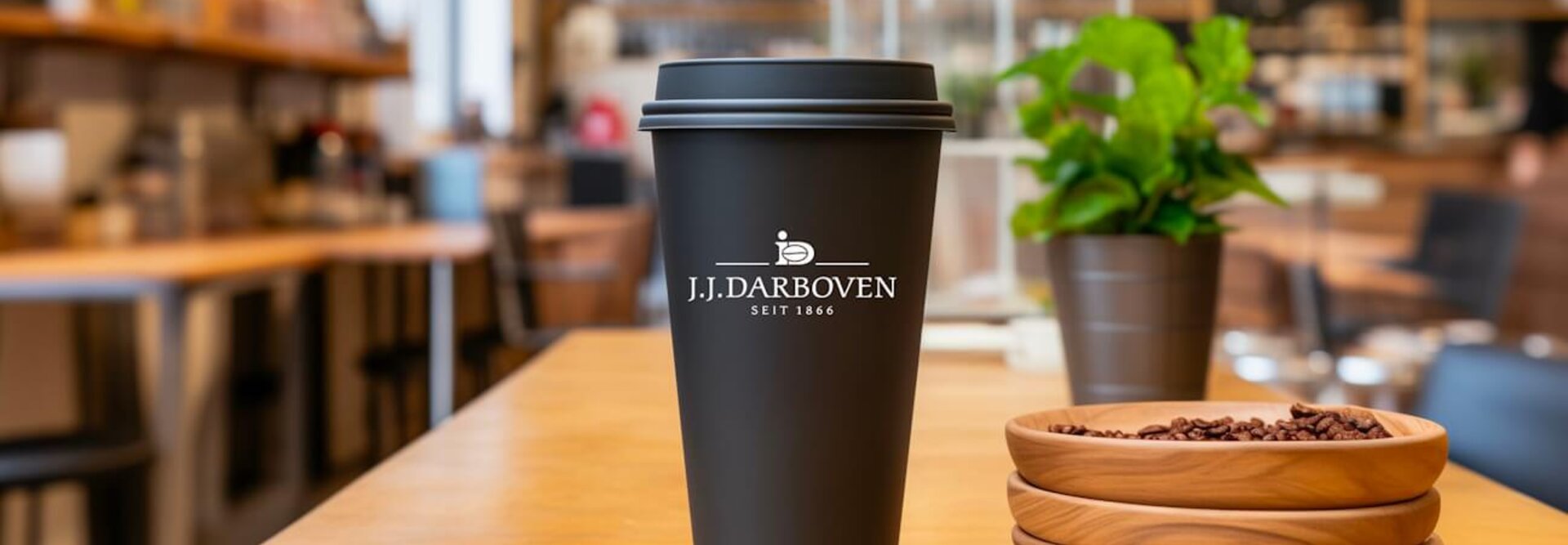 Wiederverwendbarer Kaffeebecher auf einem Holztisch, der das Branding von J.J. Darboven in einer stilvollen Caféumgebung zeigt.