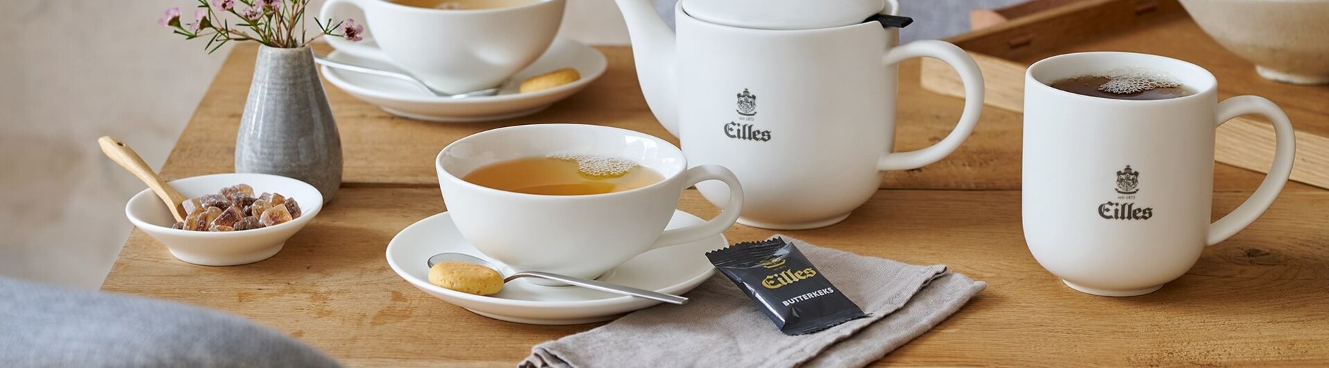 Elegant Eilles tea set with assorted teas, biscuits, and a vase of flowers on a rustic wooden table.