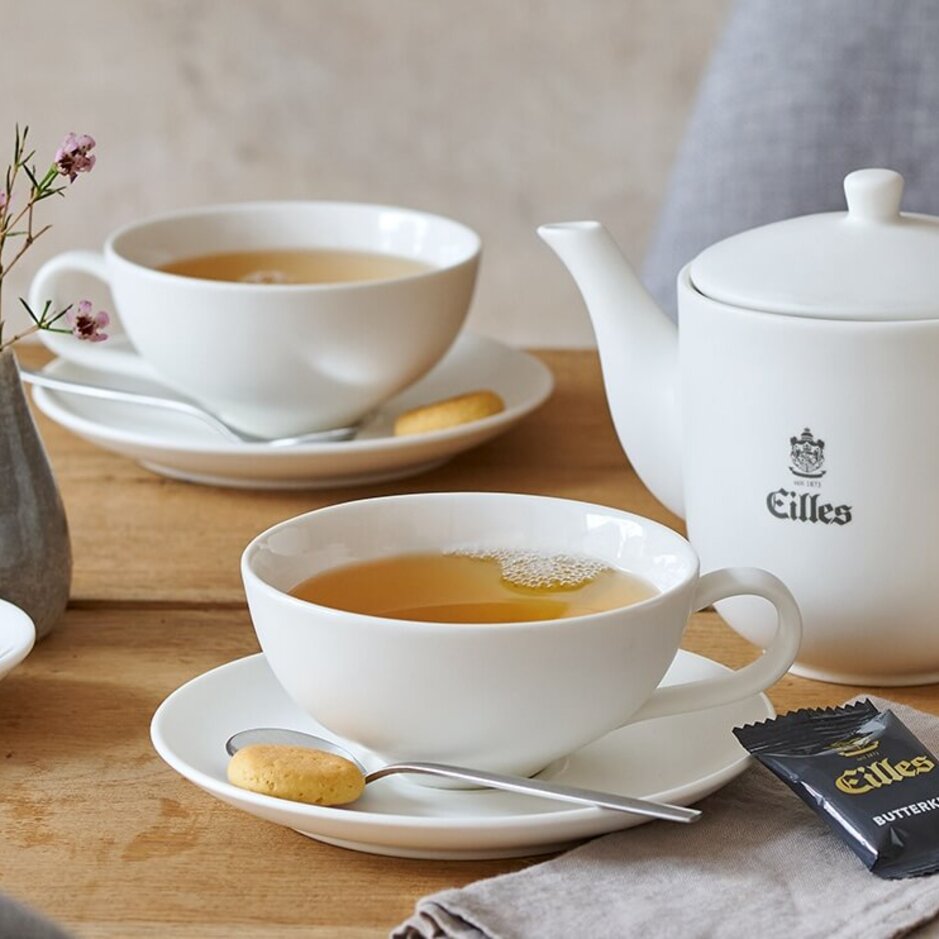 Elegant Eilles tea set with assorted teas, biscuits, and a vase of flowers on a rustic wooden table.