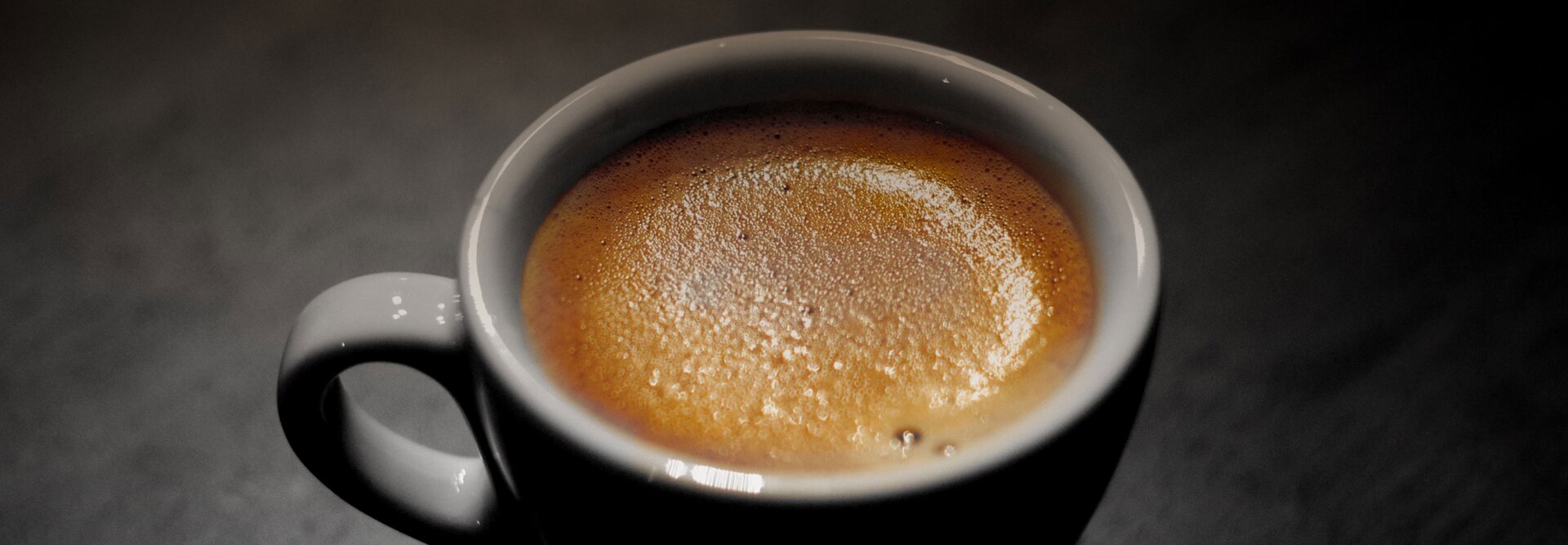 Detailný záber na šálku kávy s bohatou penou na tmavom pozadí, ktorá vytvára príjemnú atmosféru.