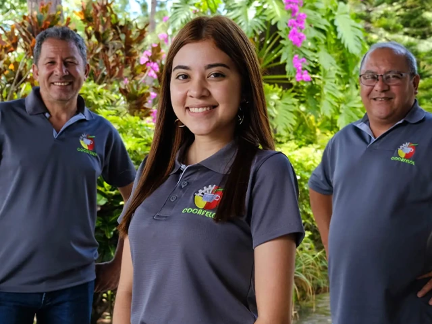 Členové týmu se společně usmívají venku a předvádějí své zářivé uniformy uprostřed bujných tropických rostlin.