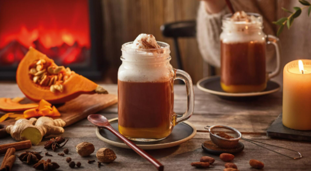 Warme Kürbisgewürzgetränke mit Schlagsahne, Gewürzen und Kerzen schaffen eine gemütliche Herbstatmosphäre am Kamin.