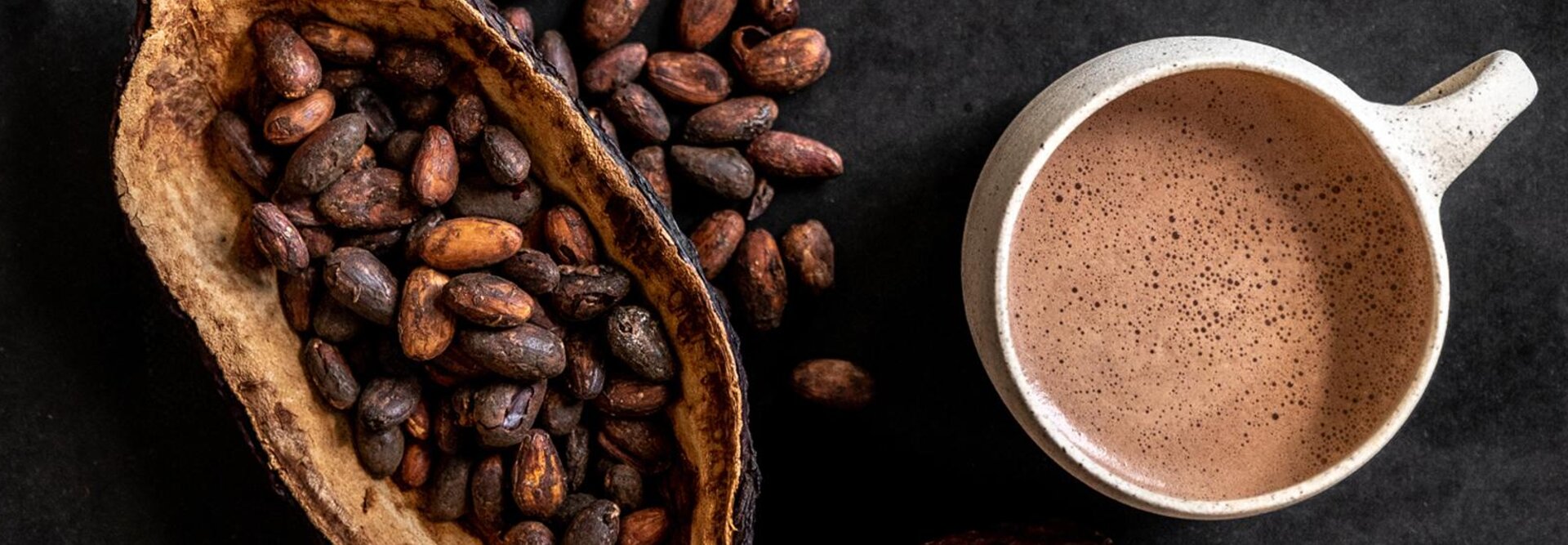 Des fèves de cacao et une tasse de chocolat riche boivent sur une surface sombre, mettant en valeur l'essence du chocolat fin.