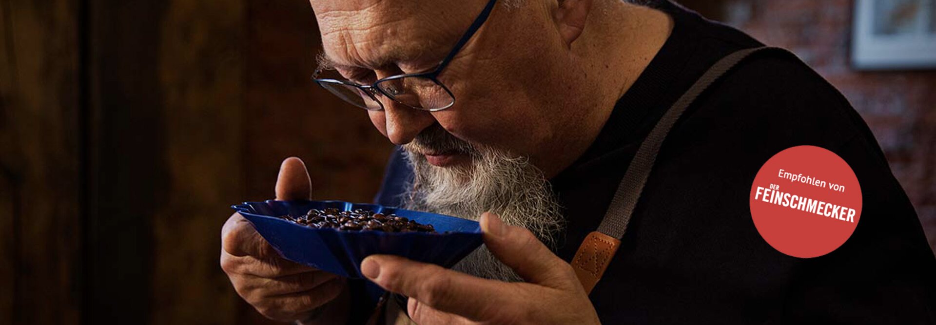 Ein fachkundiger Kaffeeverkoster bewertet die aromatischen Bohnen in einer blauen Schale, die das meisterhafte Röstverfahren von Eilles Kaffee zeigt.