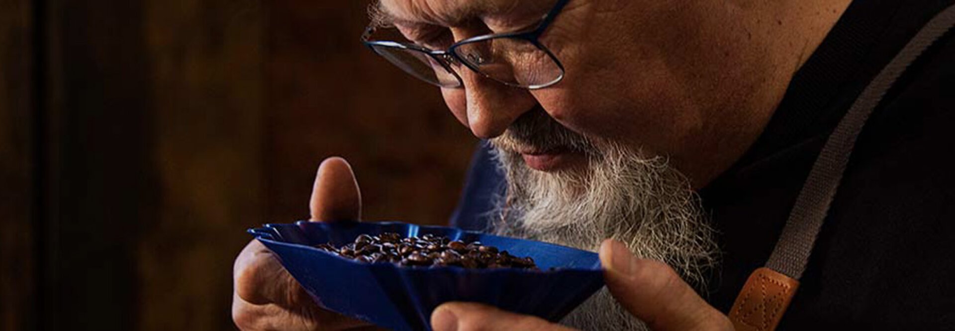 Un expert en dégustation de café évalue les grains aromatiques dans un plat bleu, mettant en valeur la maîtrise de la torréfaction d'Eilles Kaffee.