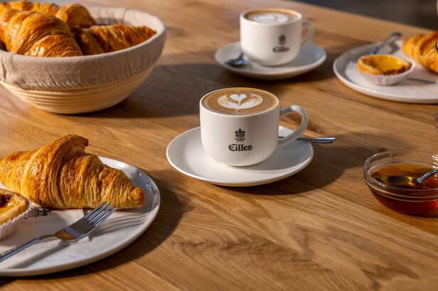 Leckere Croissants und Milchkaffee werden an einem Holztisch serviert, perfekt für ein charmantes Café-Erlebnis.