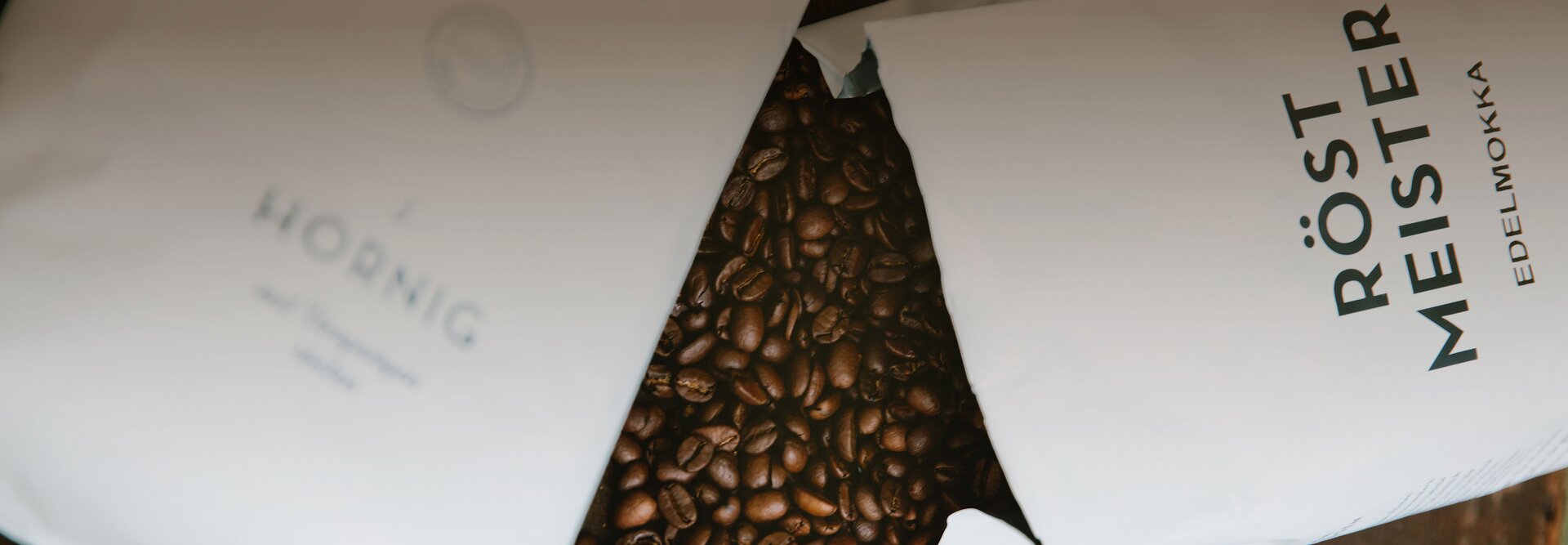 Premium coffee beans spill from Röstmeister and J. Hornig packaging, showcasing rich flavours and quality roasting.