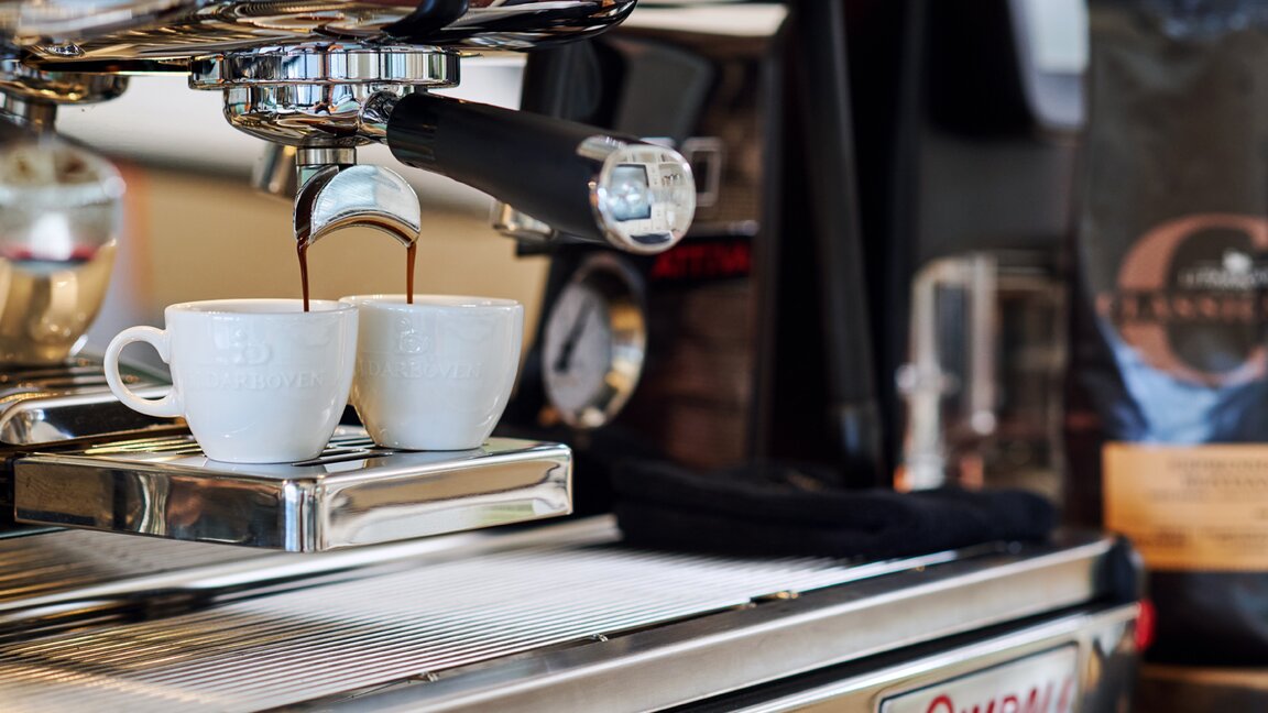 Fresh espresso pouring into two cups from a La Cimbali espresso machine, with coffee beans nearby.