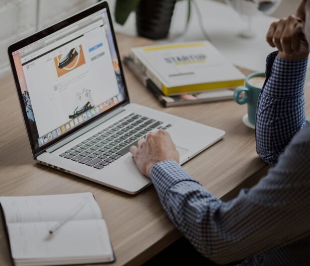 Persoon die een laptop gebruikt voor online leren, met notitieblok en koffie op een houten bureau, een moderne werkplek.