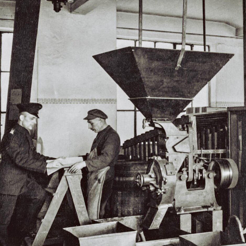 Historická scéna výroby kávy zobrazujúca pracovníkov a stroje v historickej pražiarni. Dedičstvo spoločnosti J.J. Darboven.