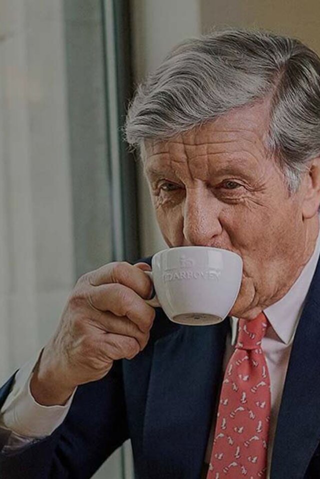 Wyrafinowany mężczyzna delektujący się kawą w kawiarni, otoczony eleganckim wystrojem i widokiem na ulicę miasta.