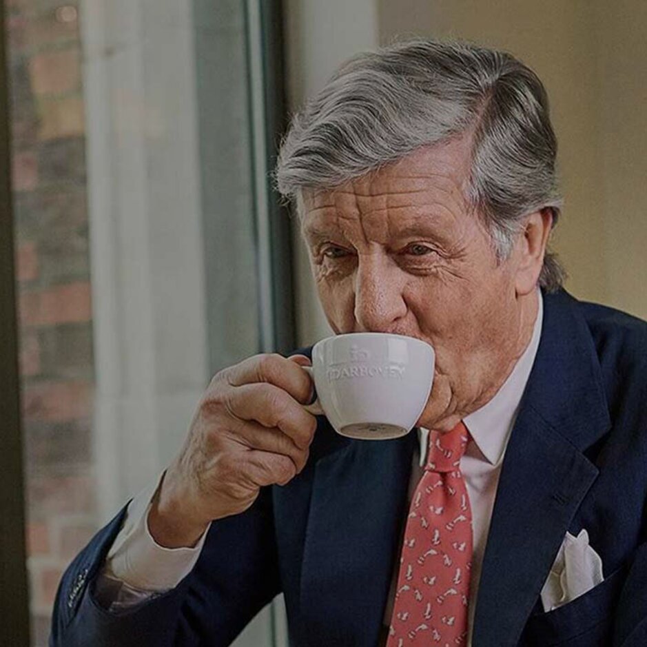 Wyrafinowany mężczyzna delektujący się kawą w kawiarni, otoczony eleganckim wystrojem i widokiem na ulicę miasta.