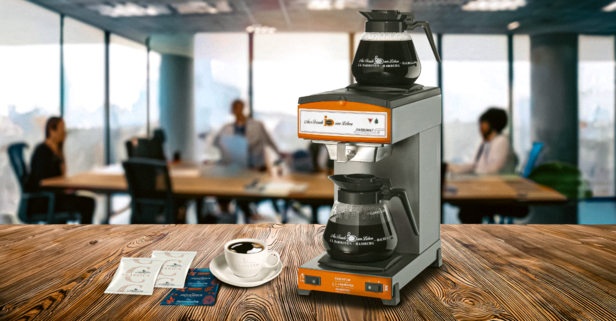 Kávovar Darbomat vaří čerstvou kávu v moderním kancelářském prostředí se šálky na dřevěném stole.