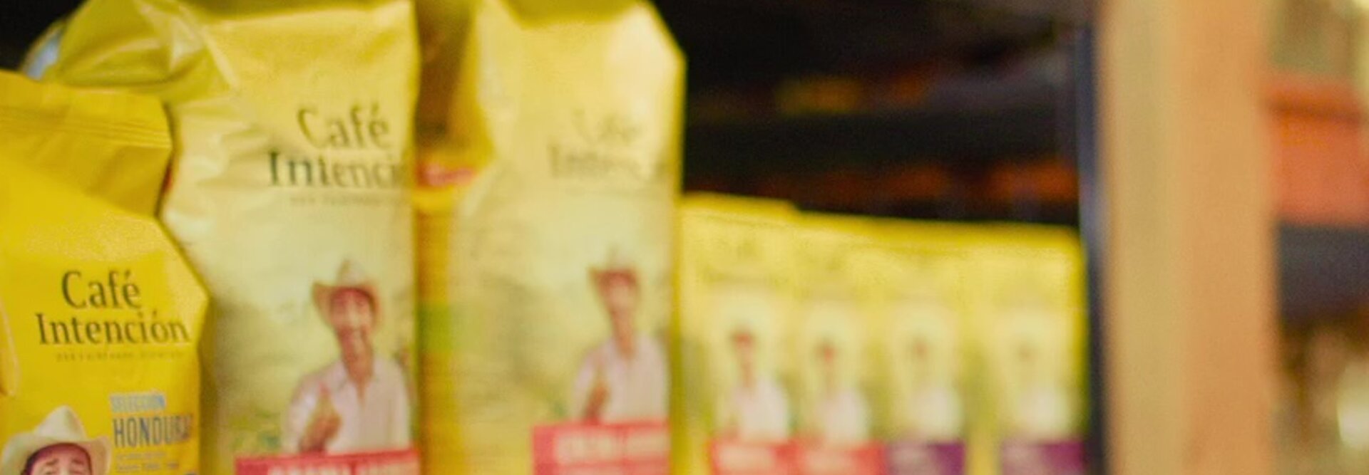 Homme en costume sélectionnant des sacs de café dans les rayons d'un supermarché, présentant une variété de marques et de saveurs.