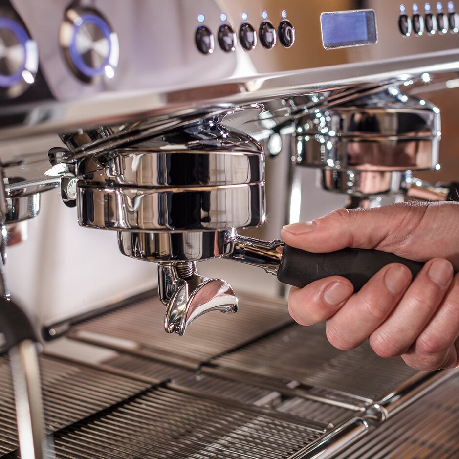 Handbedienung des Siebträgers einer Premium-Espressomaschine, die das Handwerk der Kaffeezubereitung unterstreicht.
