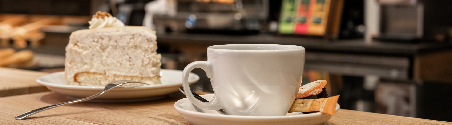 Leckerer Kuchen neben einer dampfenden Tasse Kaffee auf einem Holztisch in charmanter Café-Atmosphäre.