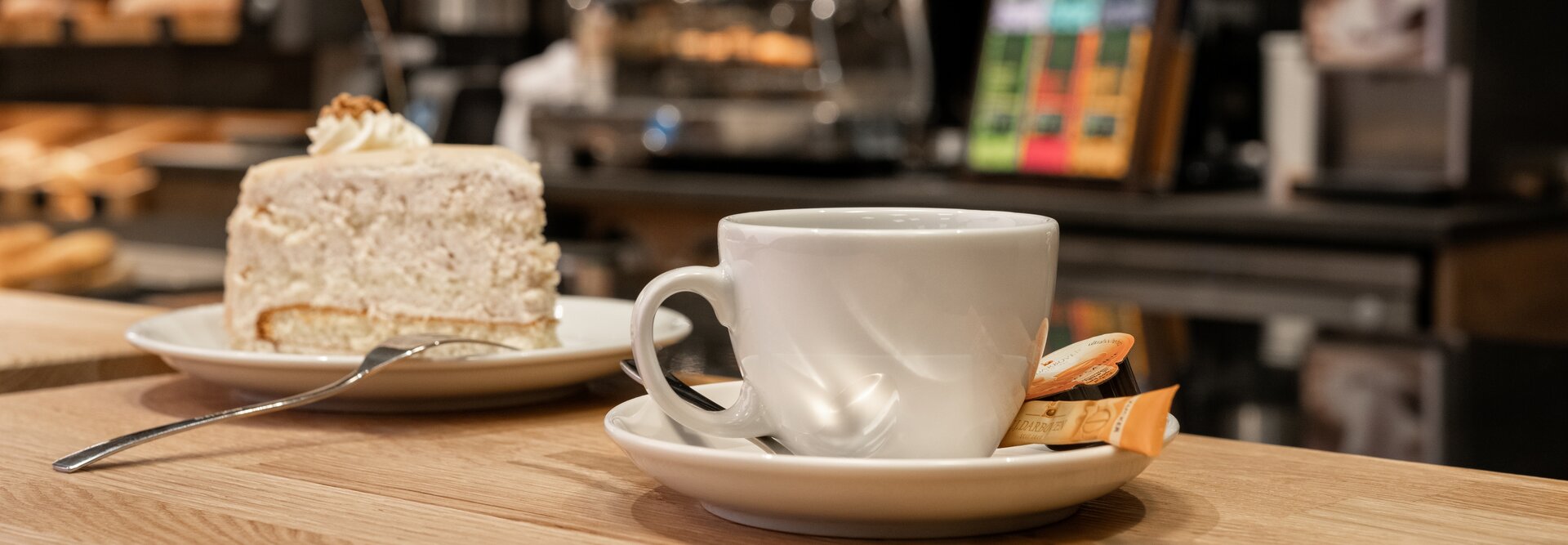 Leckerer Kuchen neben einer dampfenden Tasse Kaffee auf einem Holztisch in charmanter Café-Atmosphäre.