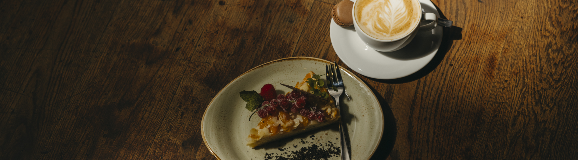 Delicious tart with fresh fruit, served alongside a latte and macaroon on a rustic wooden table.