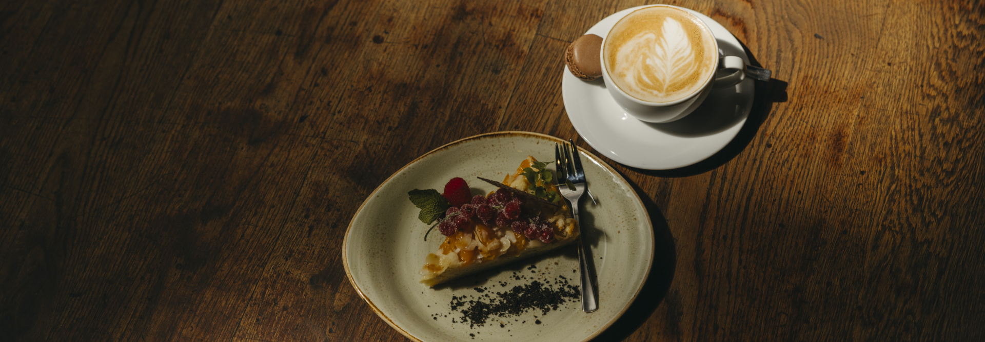 Delicious tart with fresh fruit, served alongside a latte and macaroon on a rustic wooden table.