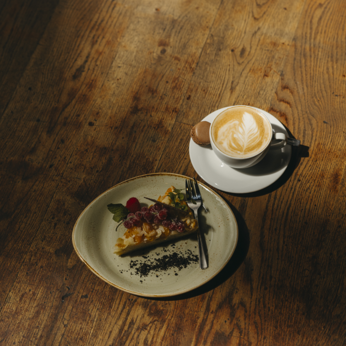 Heerlijke taart met vers fruit, geserveerd met een latte en bitterkoekje op een rustieke houten tafel.