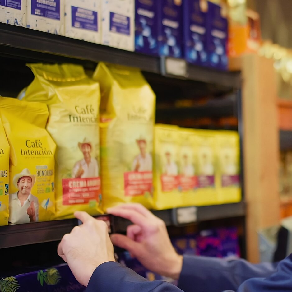 Man in a suit selecting coffee from a shelf, showcasing a variety of colourful coffee brands in a store.