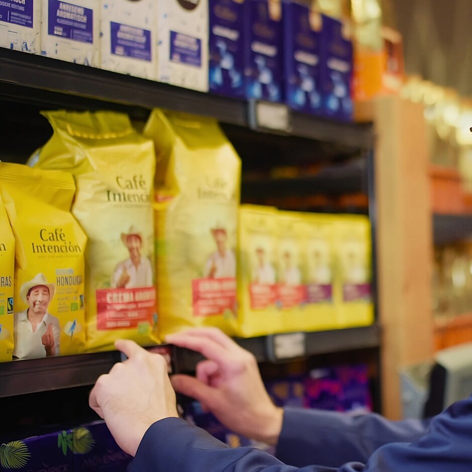 Ein Mann im Anzug wählt Kaffee aus einem Regal aus, das eine Vielzahl von bunten Kaffeemarken in einem Geschäft präsentiert.