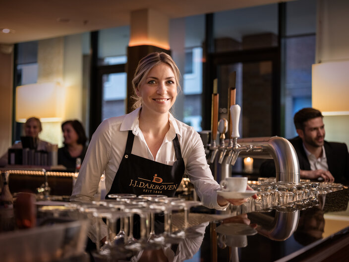 Barista servant du café chez J.J. Darboven, mettant en valeur l'excellence de l'hospitalité dans un café moderne.