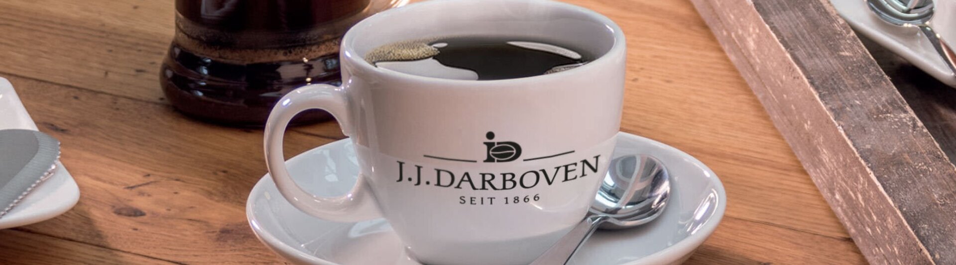 Tasse à café de J.J. Darboven posée sur une table en bois, à côté d'un petit déjeuner composé de pain, de fromage et d'un œuf.