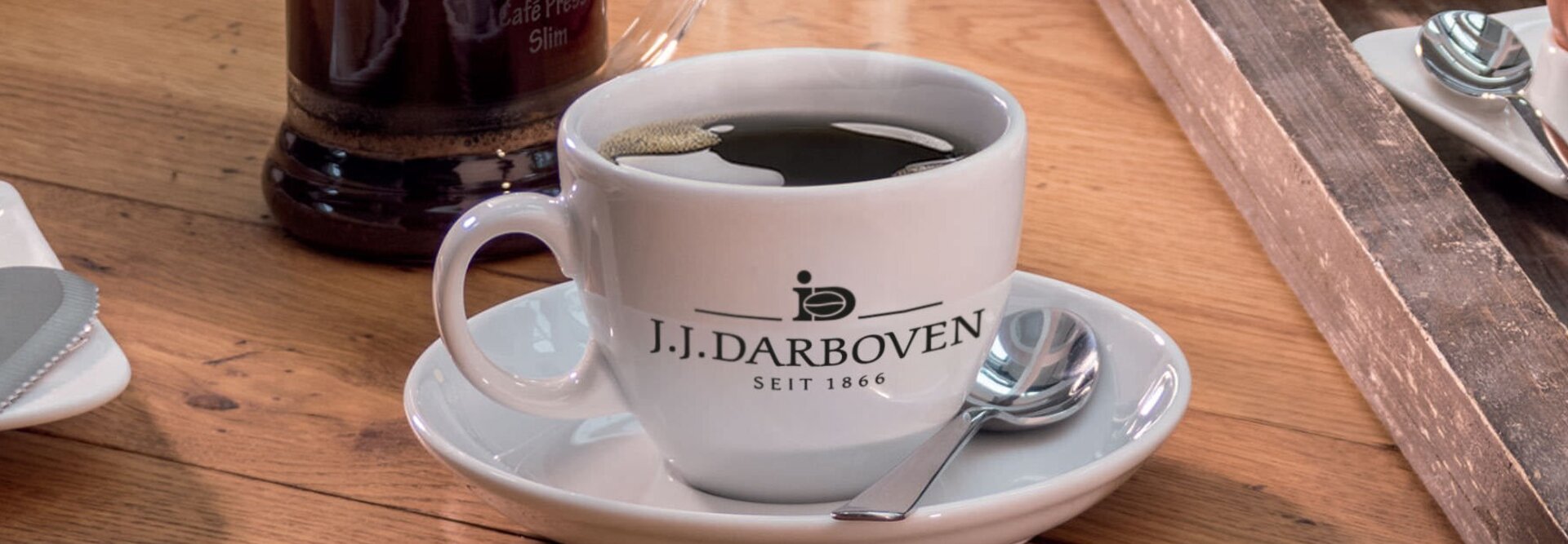 Tasse à café de J.J. Darboven posée sur une table en bois, à côté d'un petit déjeuner composé de pain, de fromage et d'un œuf.