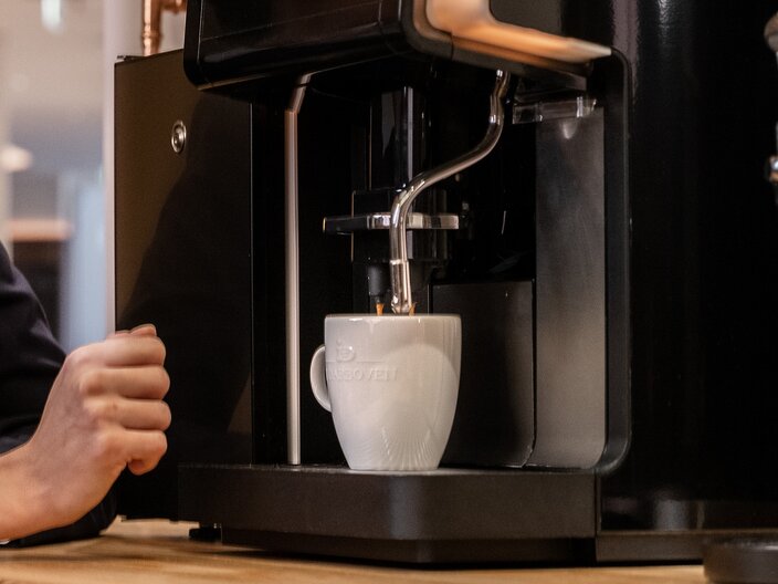 Barista preparing a cup of coffee with a sleek coffee machine in a modern café setting.