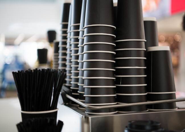 Stacks of black disposable cups and straws ready for service in a modern café setting, promoting efficient system gastronomy.