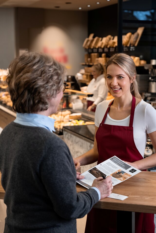 Ein freundlicher Barista bedient einen Kunden in einem modernen Café, in dem eine Auswahl an köstlichen Backwaren und Getränken angeboten wird.