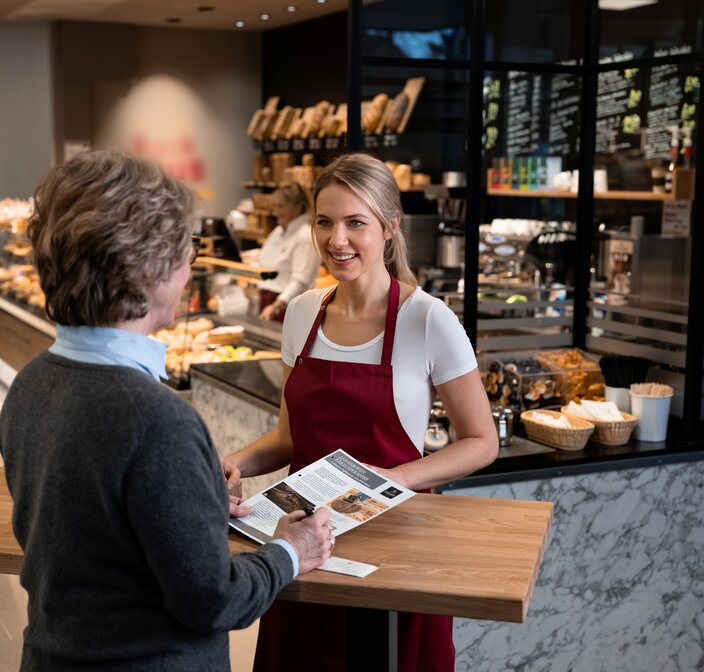 Un sympathique barista sert un client dans un café moderne, présentant une carte de délicieux produits de boulangerie et de boissons.
