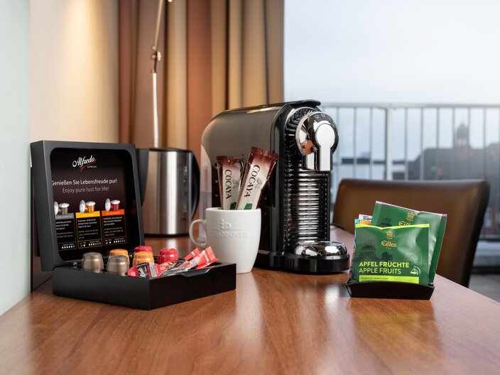 Coffee station in a hotel room featuring Nespresso machine, espresso pods, and snacks for guests' convenience.